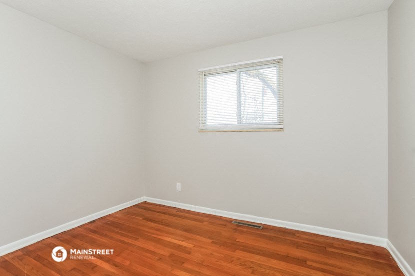 a bedroom with white walls and wood floors and a window