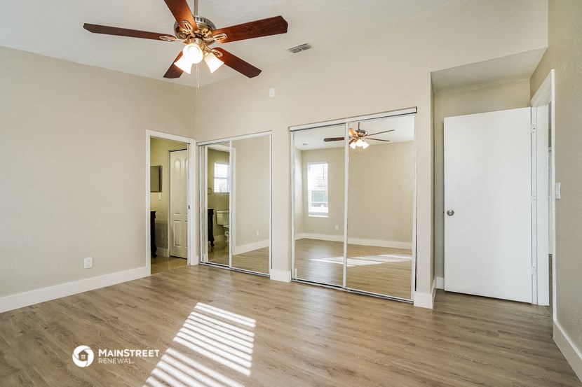an empty living room with a ceiling fan and mirrors