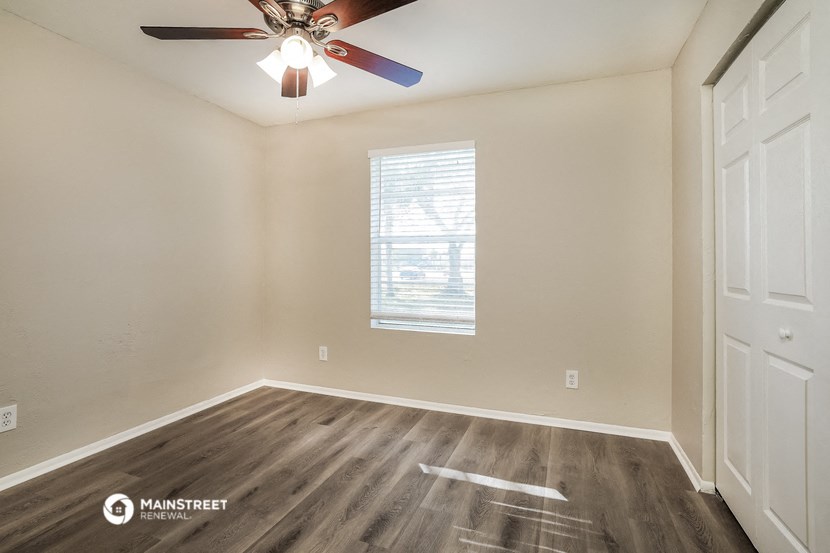 the spacious living room of an empty home with a ceiling fan