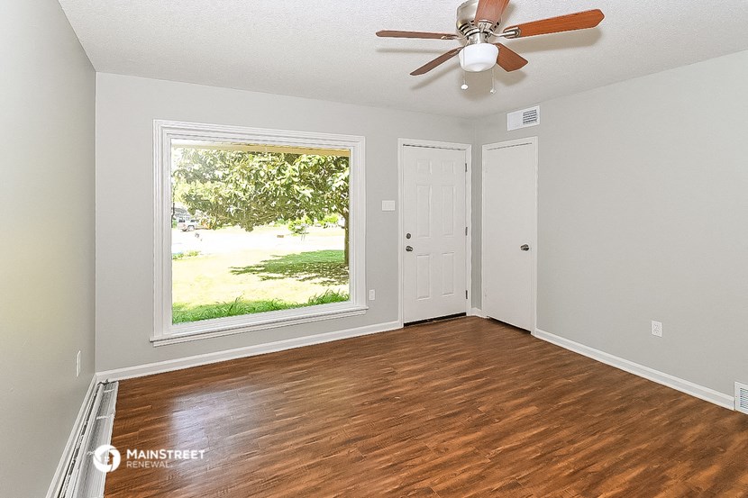 an empty living room with a large window and a ceiling fan