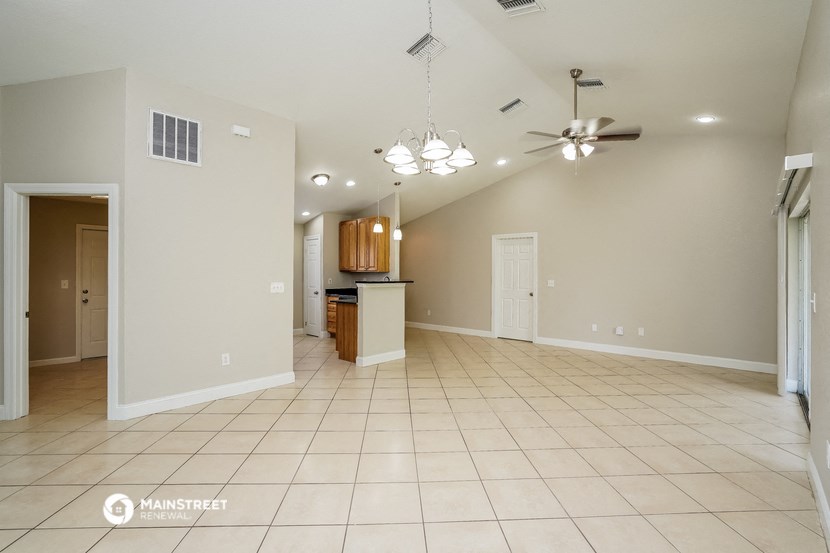 an empty living room with a kitchen in the background