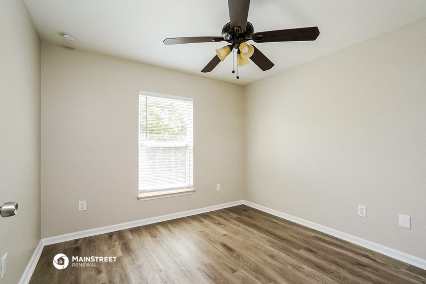 the spacious living room with wood flooring and a ceiling fan