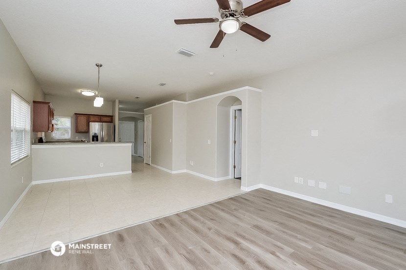 an empty living room with a ceiling fan and a kitchen
