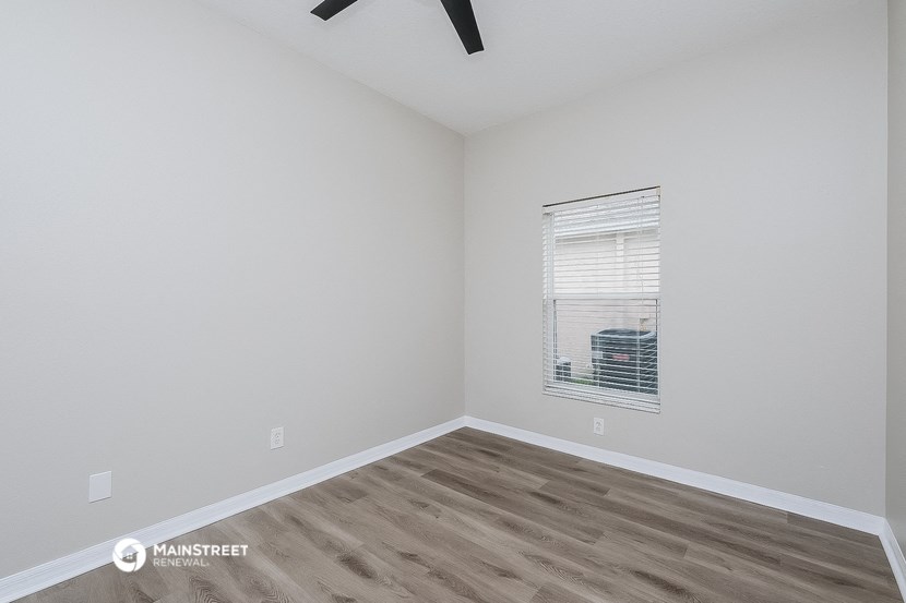 a bedroom with white walls and wood flooring and a window