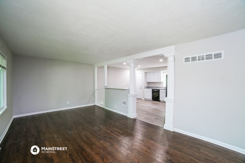 the living room and kitchen of an apartment with wood flooring and white walls