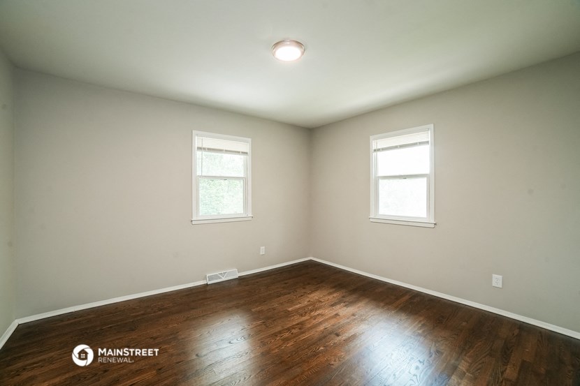 the living room of a house with wooden floors and two windows