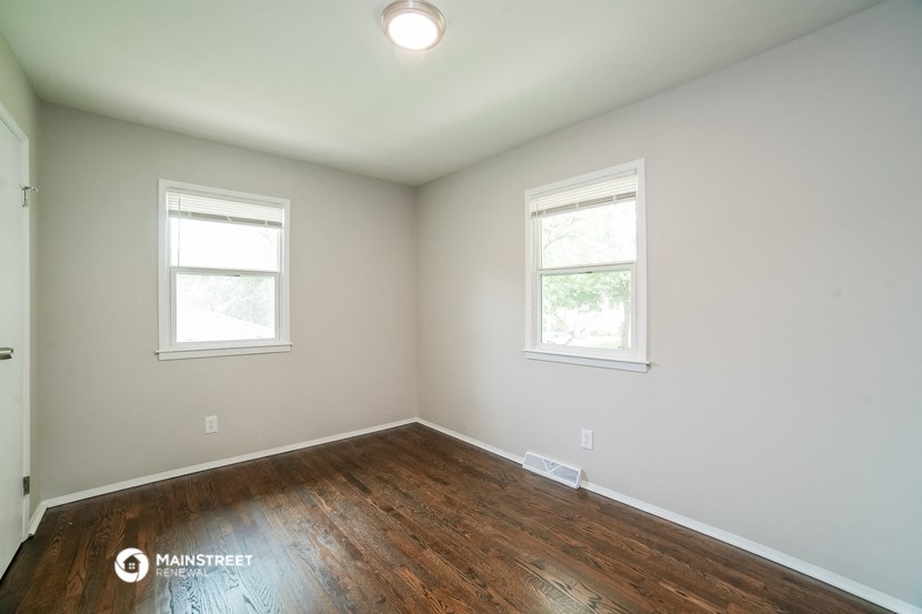 an empty room with wooden floors and two windows