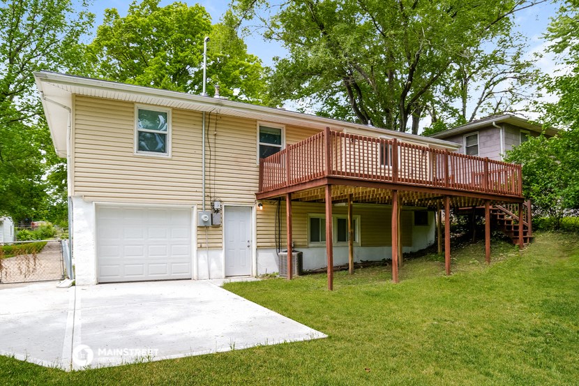 a yellow house with a deck and a white driveway