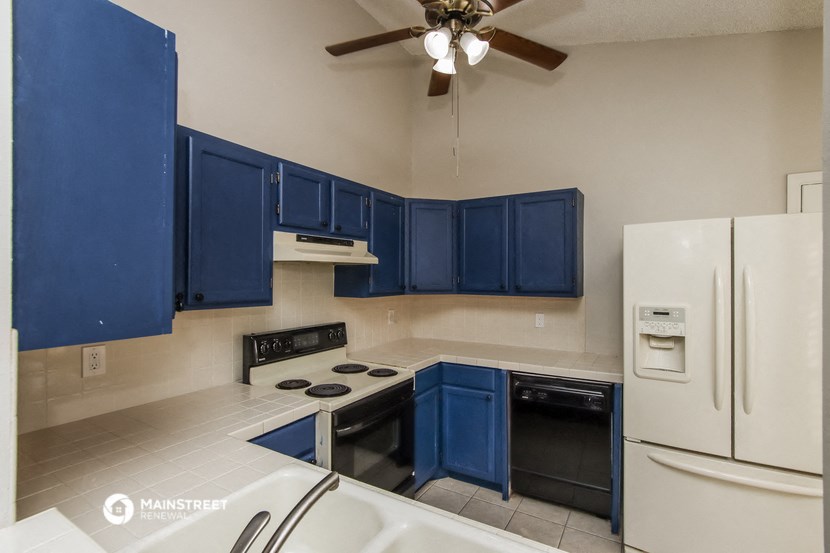 a kitchen with blue cabinets and white appliances and a ceiling fan