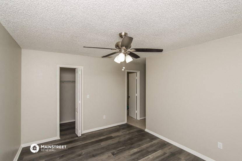 the spacious living room with ceiling fan and hallway to the bedroom