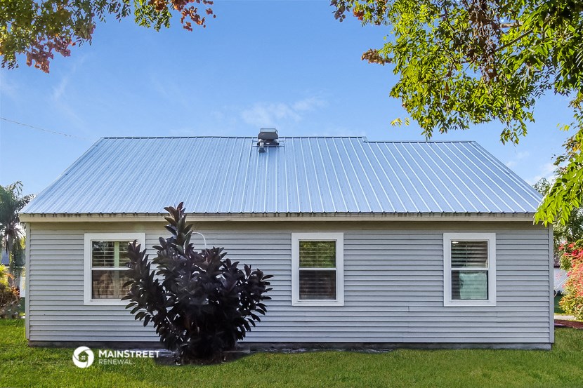 a white house with a metal roof and a purple plant