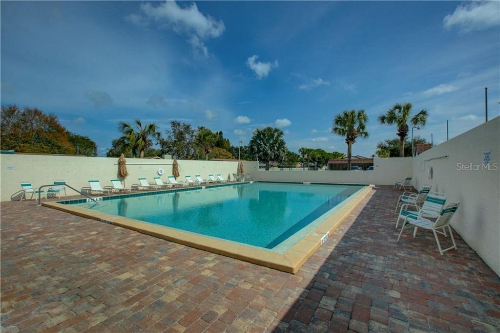 A pool surrounded by chairs and trees.