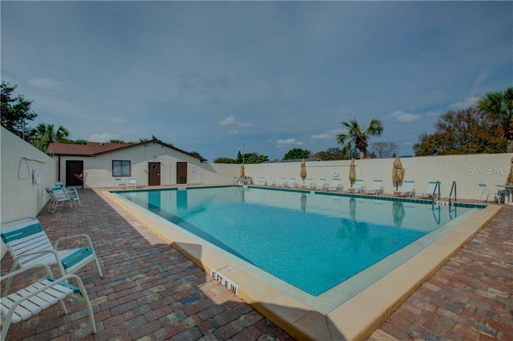A pool with a brick border and a white fence.