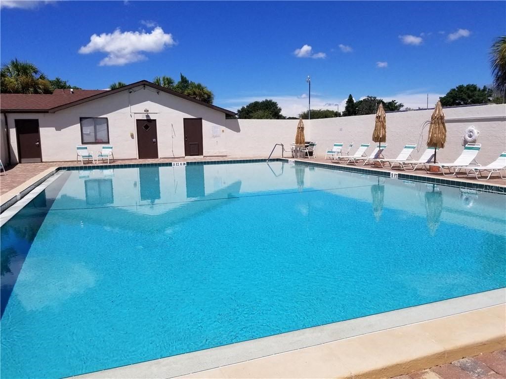 A large swimming pool with a white building and a row of lounge chairs with umbrellas.