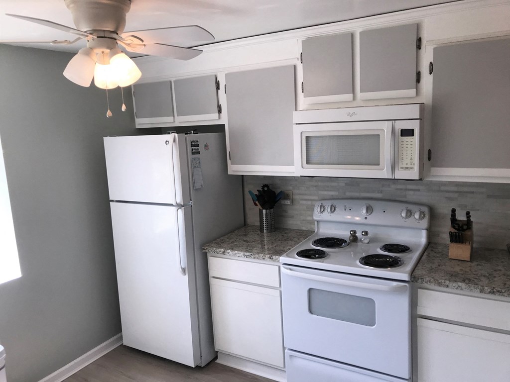 A white kitchen with a refrigerator, microwave, oven, and fan.