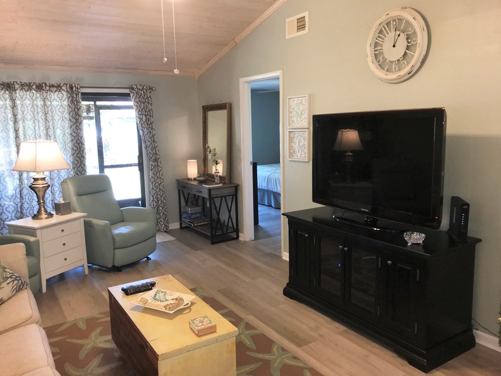 A living room with a green chair, a white dresser, a black entertainment center, and a clock on the wall.