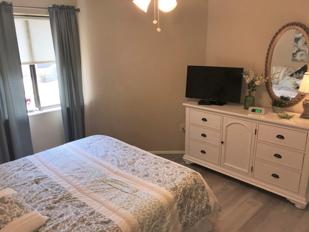 A bedroom with a bed, a dresser, and a window with curtains.