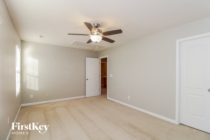 an empty living room with a ceiling fan and a door to a hallway