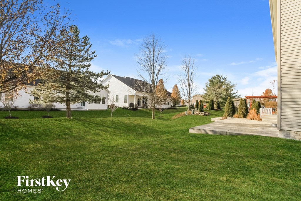 a backyard with green grass and trees and a white house