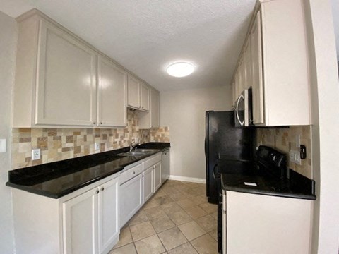 a kitchen with white cabinets and a black counter top