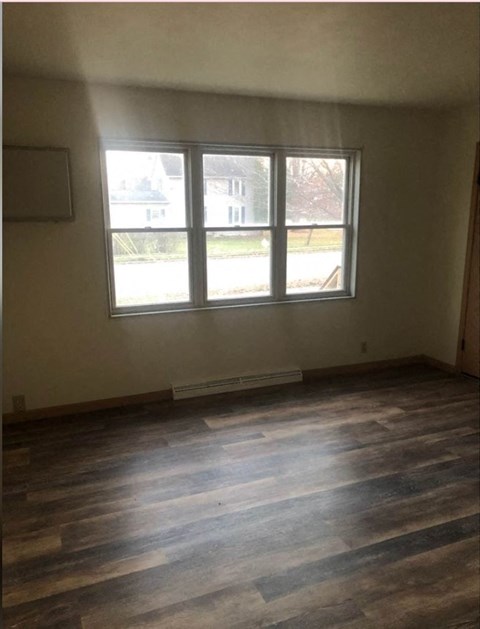 an empty living room with wooden floors and three windows