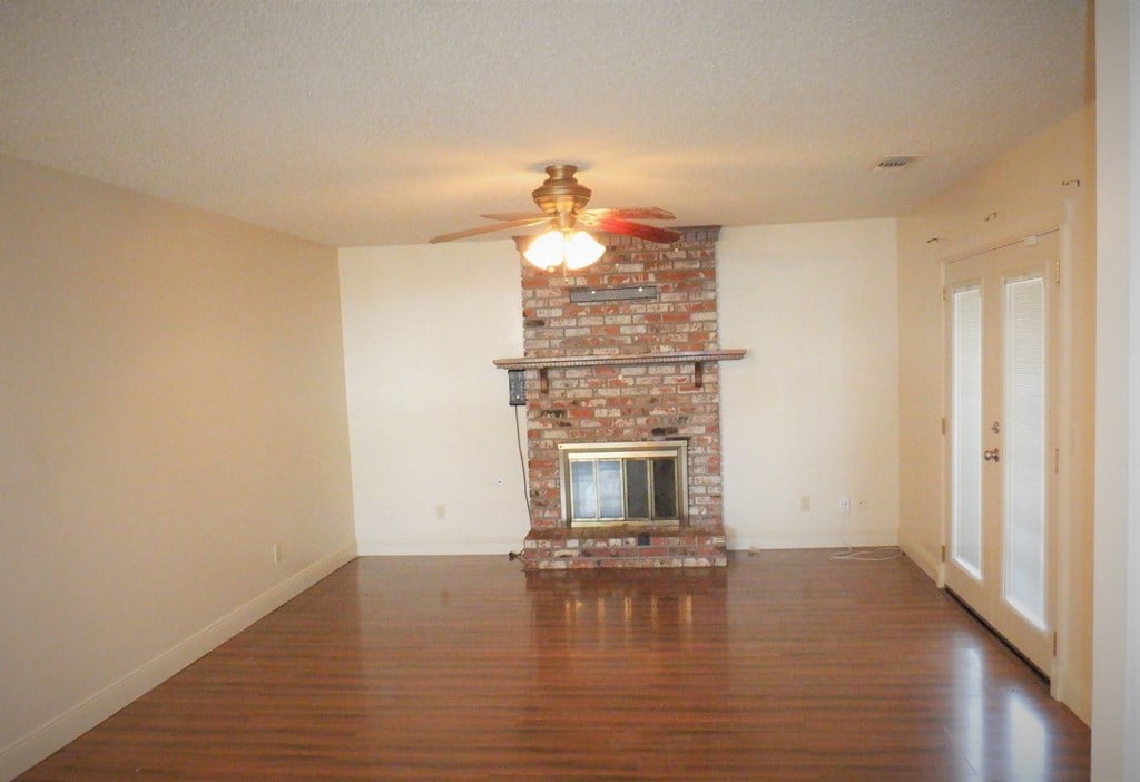 an empty living room with a fireplace and a ceiling fan