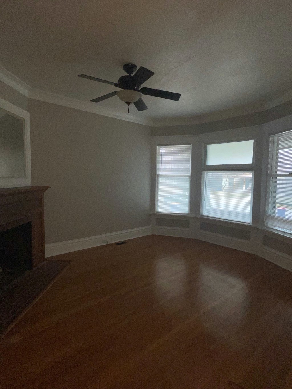 an empty living room with a ceiling fan and three windows