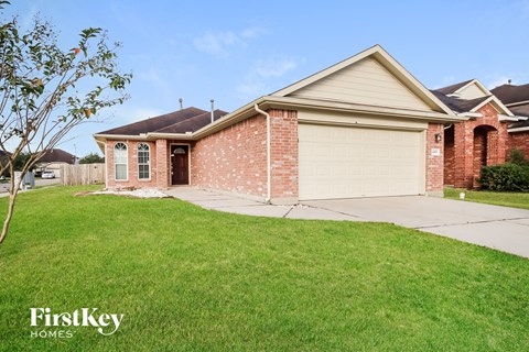 A brick house with a garage door and a tree in front.