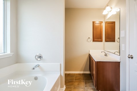 A white bathroom with a wooden cabinet and a white tub.