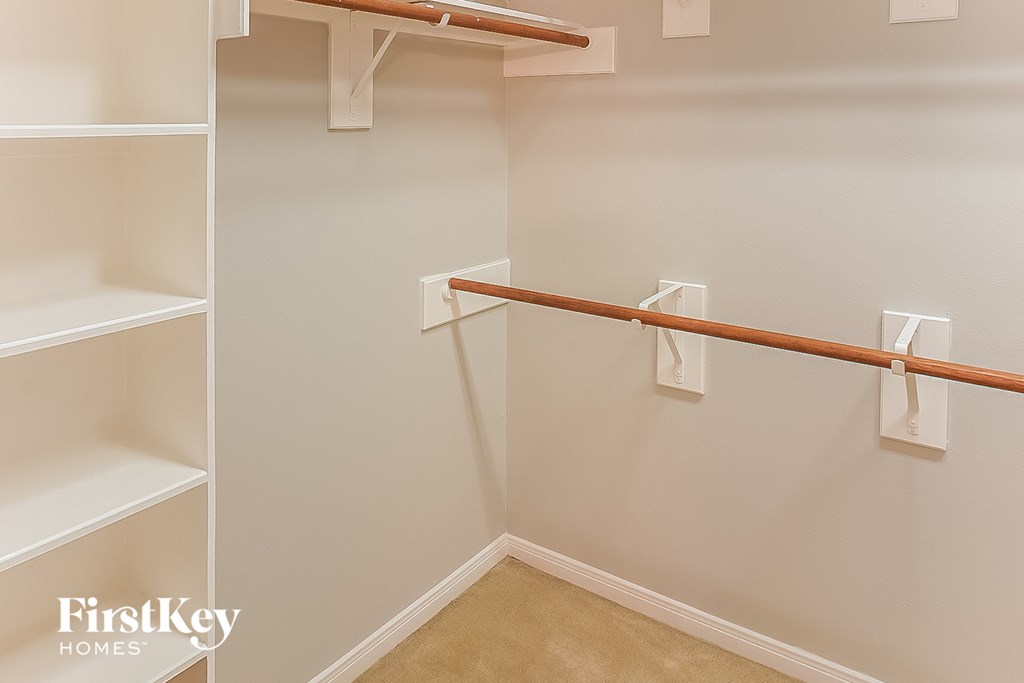 A white shelving unit with a wooden bar in a room with white walls.