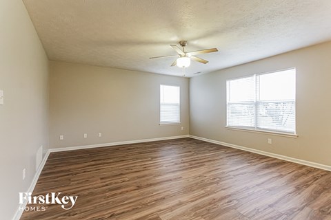 the spacious living room with hardwood flooring and a ceiling fan