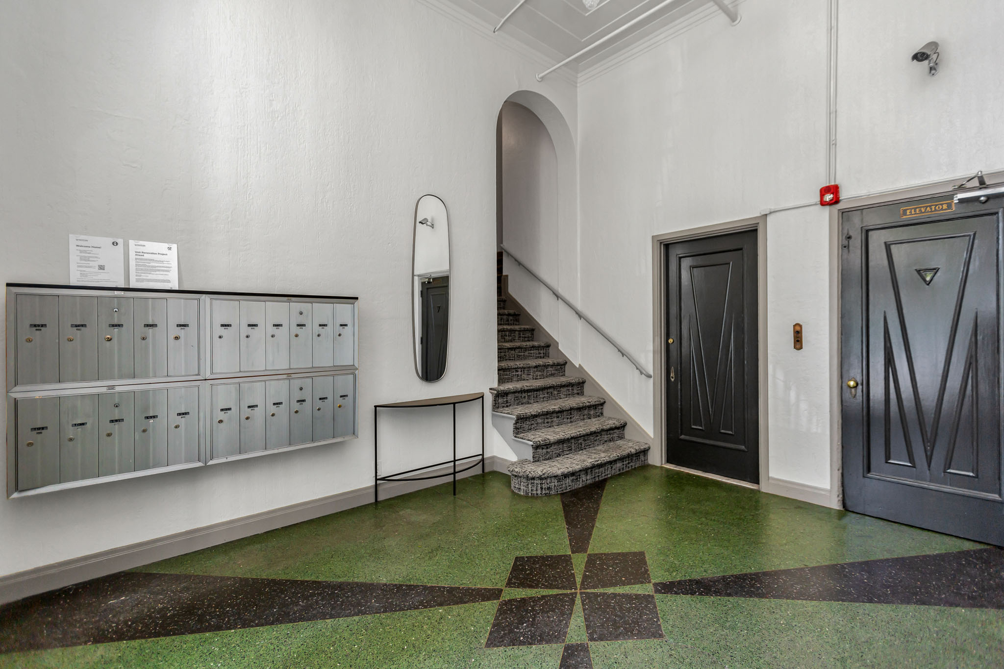 A hallway with a staircase, mailboxes, and doors.