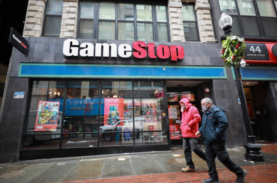 Two people walking past a GameStop store.