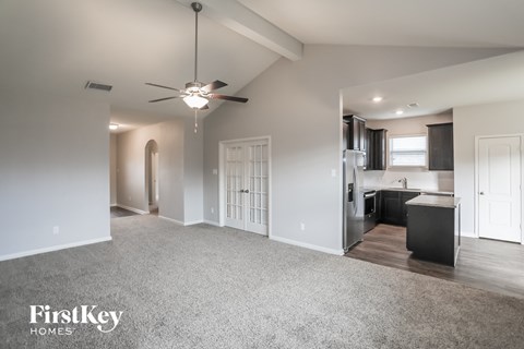 A spacious living room with a ceiling fan and a kitchen area in the background.