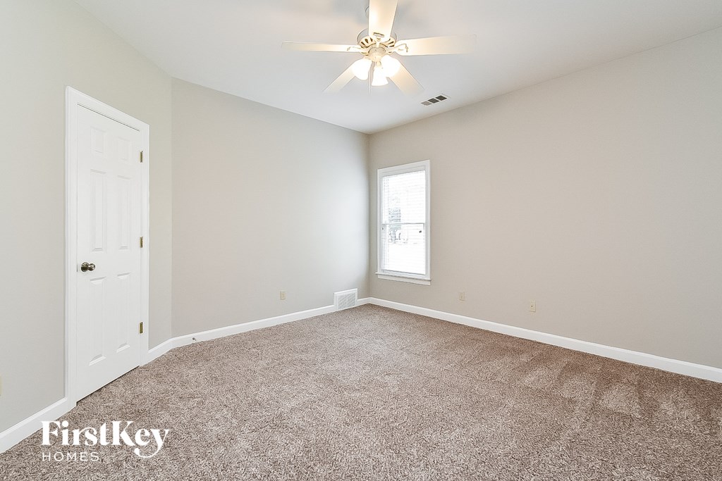 A room with a carpeted floor, a ceiling fan, and a window.