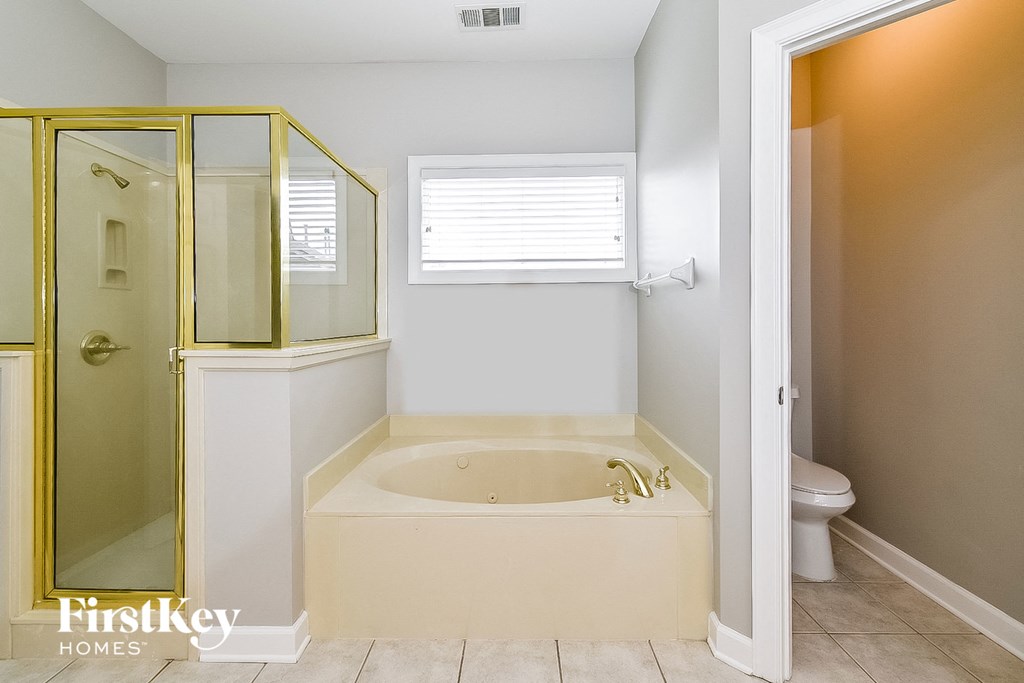 A bathroom with a gold shower stall and a white bathtub.