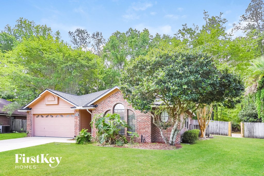 A house with a garage is surrounded by greenery and has a tree in front of it.