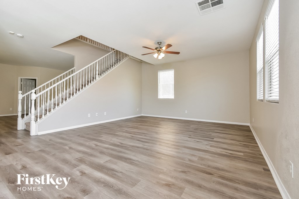 an empty living room with a ceiling fan and a staircase