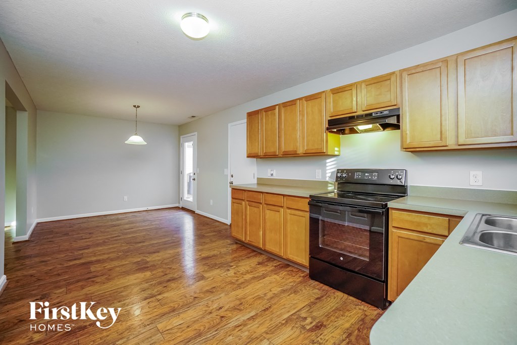 an empty kitchen with wood flooring and a black stove and oven