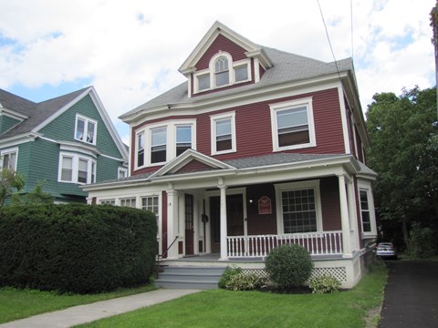 a red and white house with a porch and a green house next to it