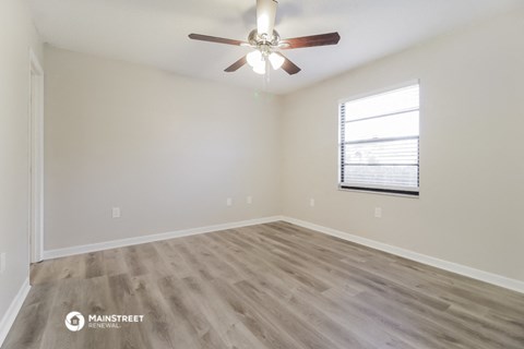 the spacious living room with hardwood flooring and a ceiling fan