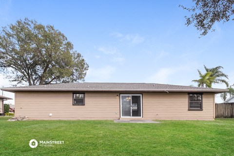a small tan house with a grassy yard and a tree