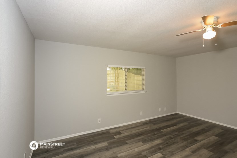 the spacious living room with wood flooring and a ceiling fan