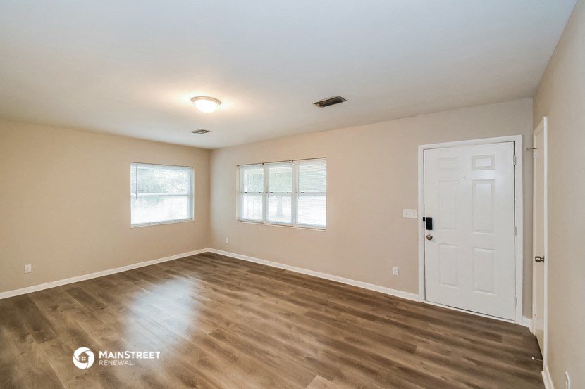the spacious living room with a white door and wood flooring