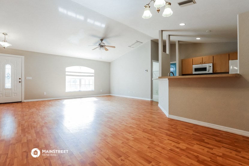 an empty living room with wood flooring and a kitchen