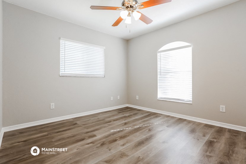 the spacious living room with hardwood flooring and a ceiling fan