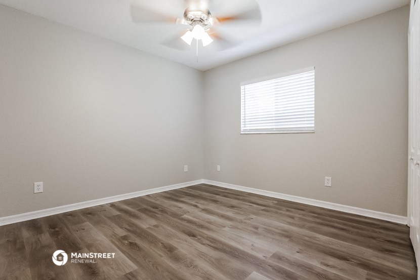 the spacious living room with wood flooring and a ceiling fan