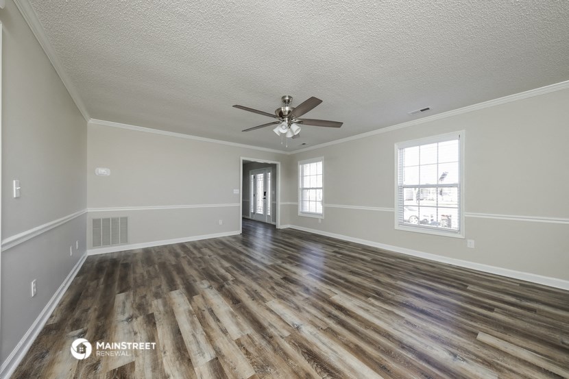 the spacious living room with hardwood flooring and a ceiling fan
