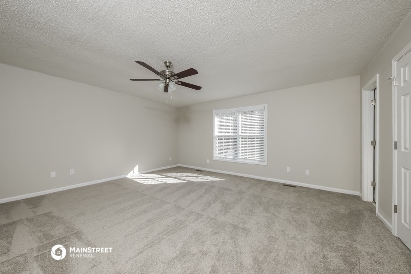 the spacious living room with ceiling fan and carpeting