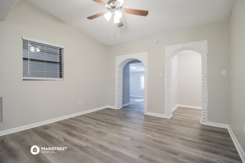 an empty living room with a ceiling fan and a door to a hallway